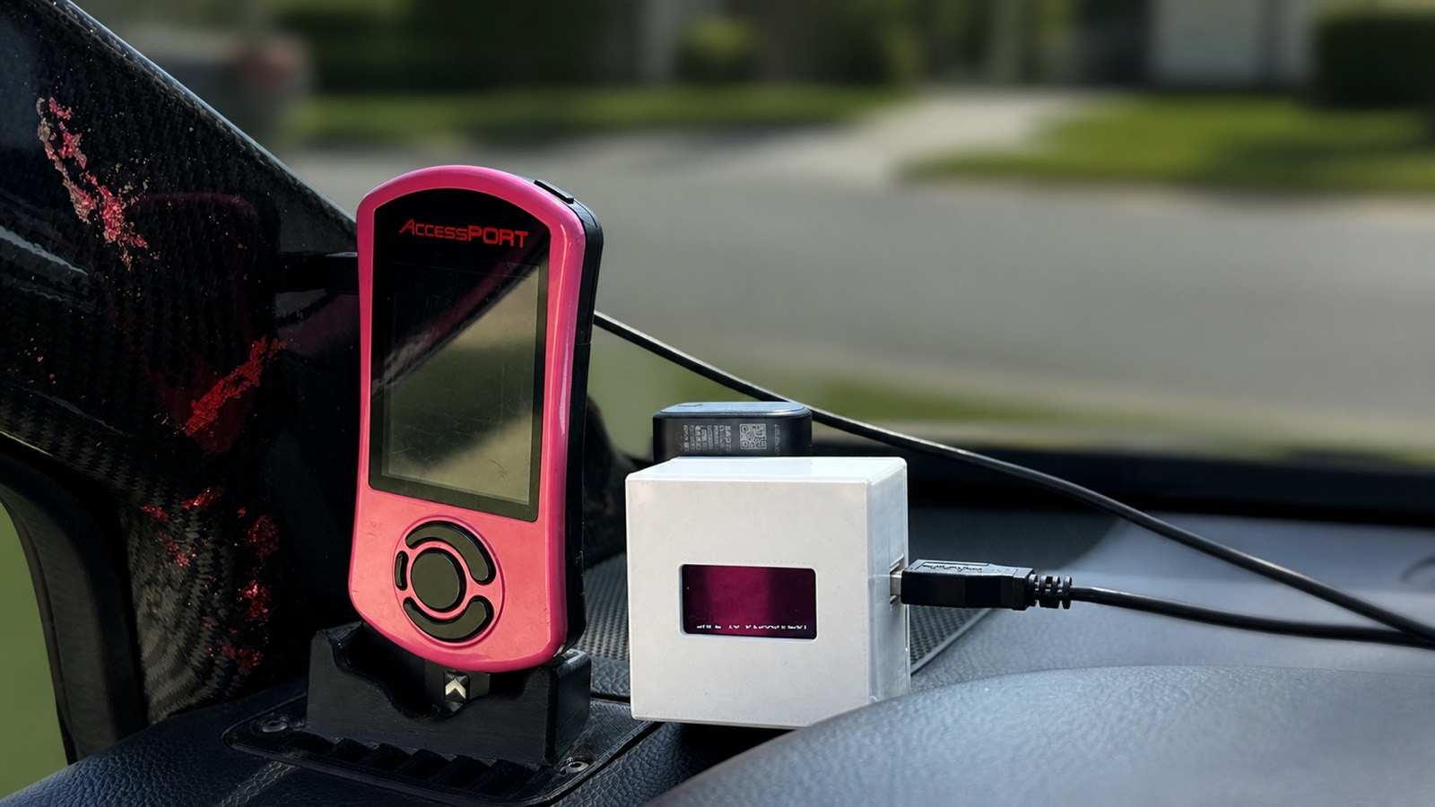 A RevLink Sidecar in a printed white case sitting on a car's dashboard next to a pink COBB AccessPort, connected by a USB cable.